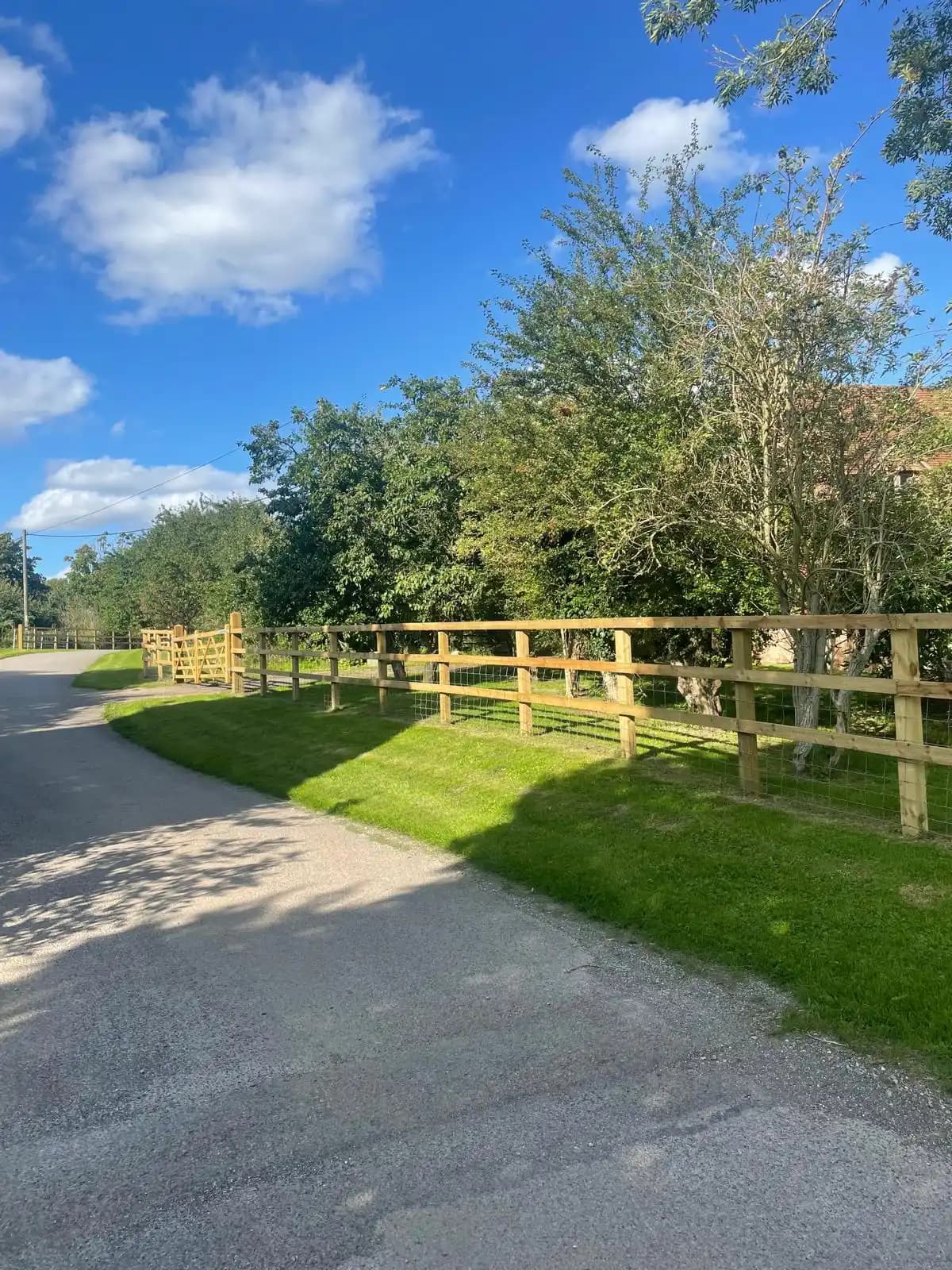 Post and rail driveway fence beside a lane under blue sky