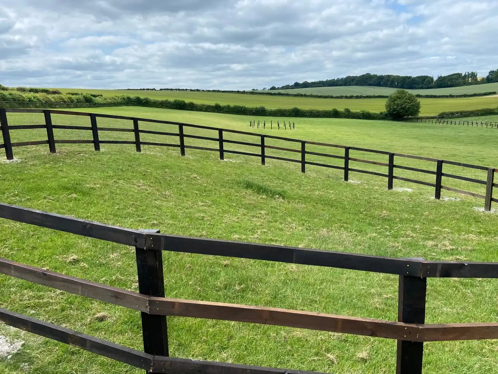 Black post and rail field fence across open countryside