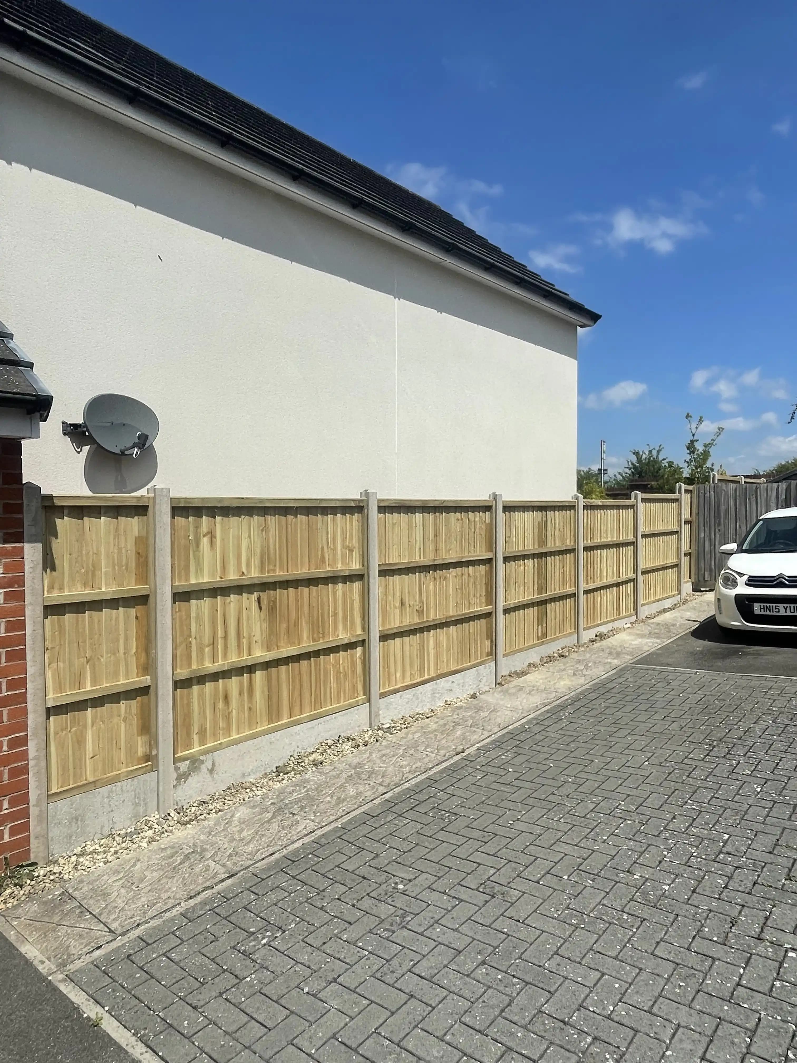 Closeboard fence beside a driveway and white rendered house