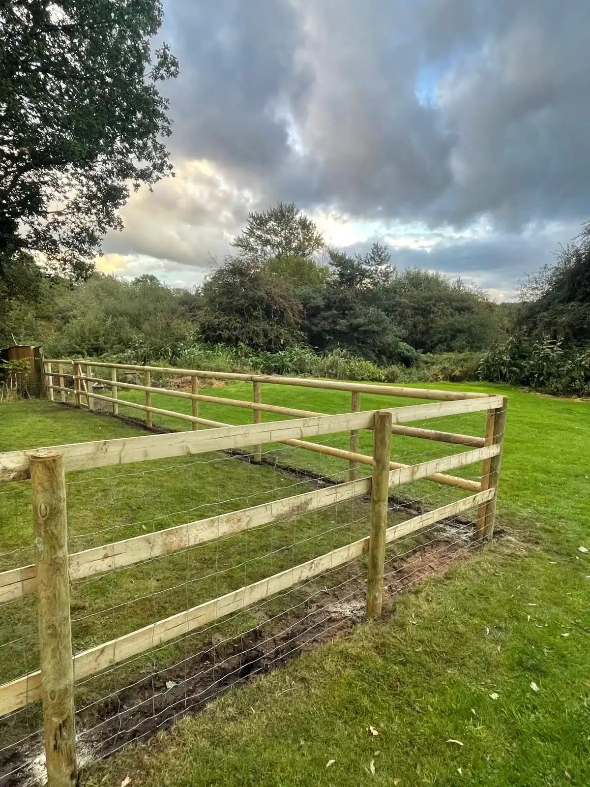 Post and rail fence across a rural garden with cloudy sky