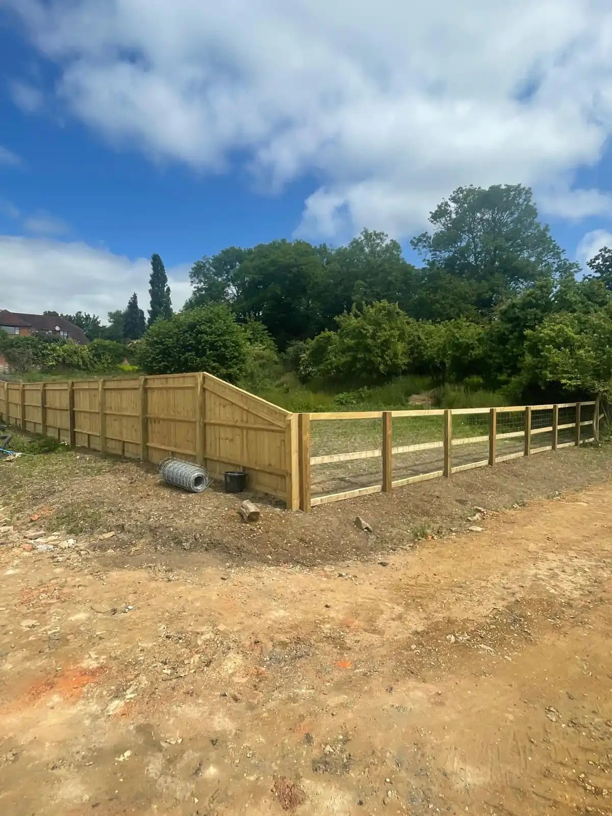 Post and rail fence around a sandy garden area under blue sky