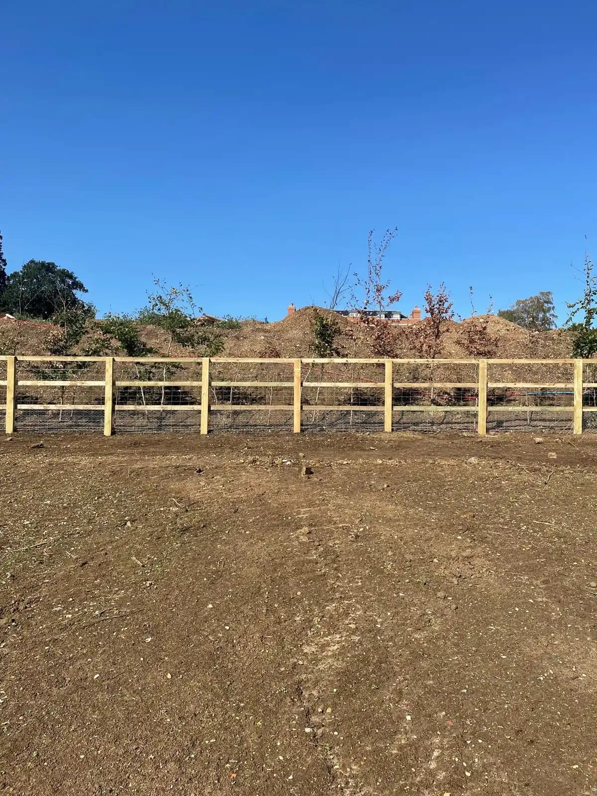 Post and rail fence around a sandy paddock under blue sky