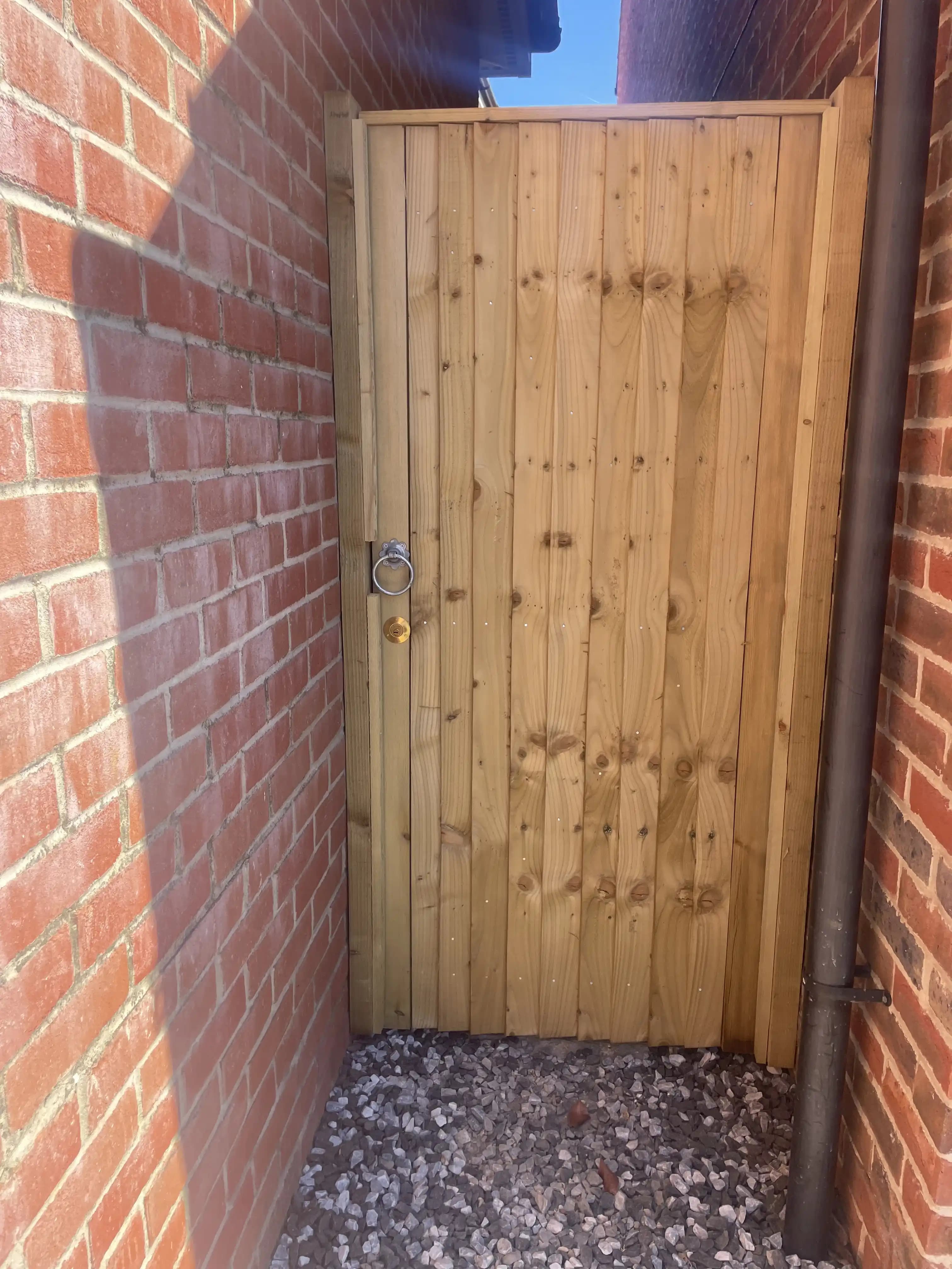 Timber side gate fitted between red brick walls