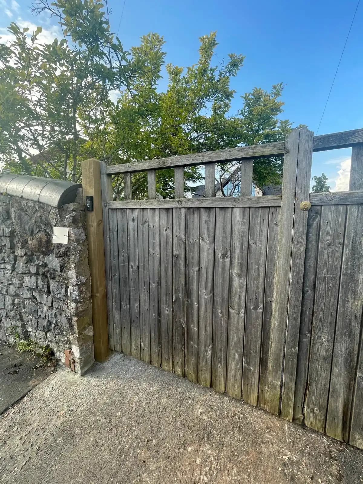 Timber side gate fitted beside a stone wall under blue sky